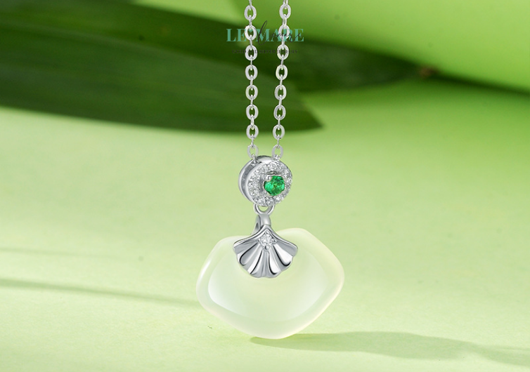 Ngọc Phiến – Làn quạt ngọc nâng niu quyền quý BNDC29 Không lấp lánh như kim cương, không kiêu sa như hồng ngọc, ngọc bích lặng lẽ tỏa sáng theo cách riêng: thâm trầm, dịu mát, như một dòng suối bình yên chảy giữa lòng đá. Qua hàng triệu năm, viên ngọc được chắt lọc từ tinh khí núi rừng đã trở thành bảo vật trong văn hóa phương Đông, tượng trưng cho sự an nhiên, thuần khiết và trường tồn.Trong “Ngọc Phiến”, viên ngọc ấy được đặt giữa lòng một chiếc quạt tay cách điệu – nhẹ nhàng, uyển chuyển – như một nàng thiếu nữ e ấp sau vành quạt, ánh mắt khẽ nghiêng, giấu nửa nụ cười quyền lực.