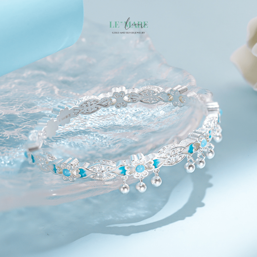 Thanh Vi – Vòng Tay Bạc Nữ Mang Hơi Thở Hoa Lam Nhẹ Nhàng và Thanh Khiết BNVT103 Vòng tay bạc nữ Thanh Vi là món quà dành cho người phụ nữ biết yêu sự tĩnh lặng, biết tìm thấy vẻ đẹp trong điều giản dị. Chiếc lắc tay ấy không phô trương, không ồn ào, nhưng mỗi khi bạn khẽ xoay cổ tay, ánh bạc lấp lánh sẽ vẽ nên một vũ điệu nhỏ của ánh sáng và sắc hoa.Thanh Vi khiến người ta nghĩ đến người phụ nữ không cần phải lên tiếng để được chú ý – chỉ cần hiện diện đã đủ khiến không gian trở nên mềm mại hơn.